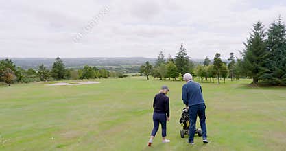 Golf players walking with clubs and talking on golf course on cloudy day, copy space