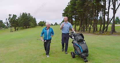 Male golf players walking with clubs and talking on golf course on cloudy day