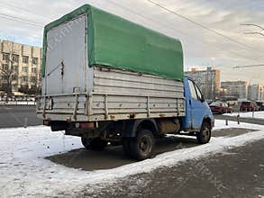 A snow-covered street hosts a used delivery truck, parked near buildings with power lines overhead The trucks white cab