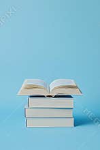 Four stacked books with one open on top against a blue background