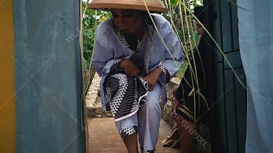 Crouching figure in traditional attire by window