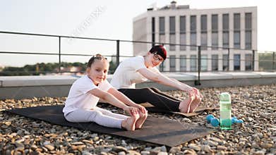 Mother and daughter stretching exercises on rooftop during sunny morning