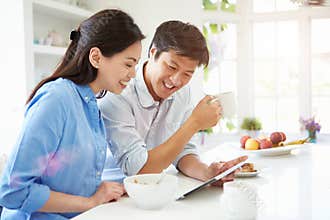 Asian Couple Looking At Digital Tablet Over Breakfast