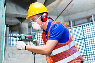 Asian worker drilling in construction site wall