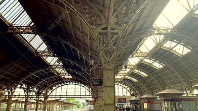 A busy train station with an expansive metal roof, showing trains and people in motion