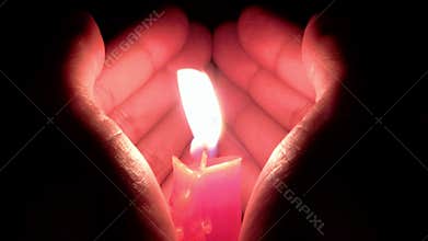 Hands shape like a heart to protect a burning candle