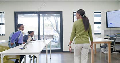 Teacher with female children opening door, high fiving and placing backpacks at desks for class