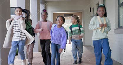 Diverse preteens emerging from schoolyard running toward camera backpacks swinging heading to class