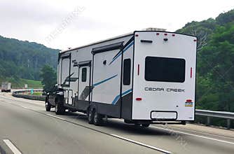 Pennsylvania, U.S.A - Jul 18, 2026 - A white Cedar Creek fifth-wheel trailer towed by a pickup truck along a scenic highway