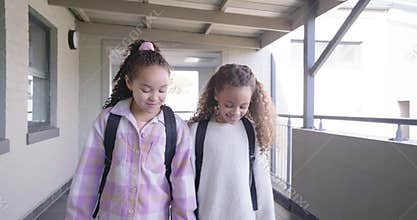 African American preteen girls entering doorway at school walking with black backpacks sharing joke