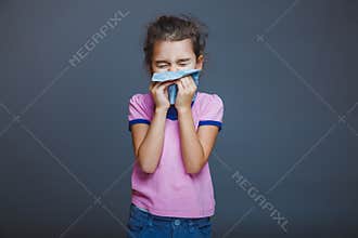 Girl child sneezes into handkerchief on a gray