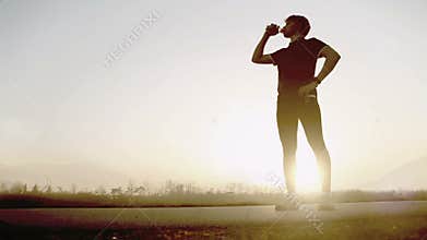 Marathon runner drinks water on the wide angle mountain landscape