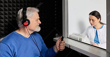 Audiologist doing hearing check-up to senior man in soundproof audiometric booth. Hearing loss treatment