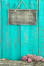 Blank rustic sign hanging on antique teal blue wood fence with log and pink flower border