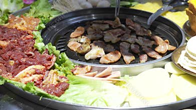 Korean BBQ grill with marinated meat, sausages, and side dishes
