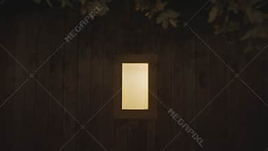 Glowing window of a wooden cabin with camera slowly pushing in at night