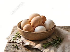An assortment of fresh eggs fills a rustic bowl presented with culinary herbs and a vintage spoon on a textured wooden