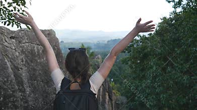 Woman tourist standing on the edge of beautiful canyon, victoriously outstretching arms up. Young female hiker with