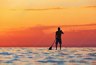 Black sunset silhouette of paddle boarder standing on SUP