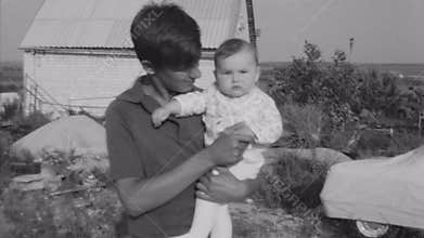 Old vintage black and white film young man holding baby in hands at village
