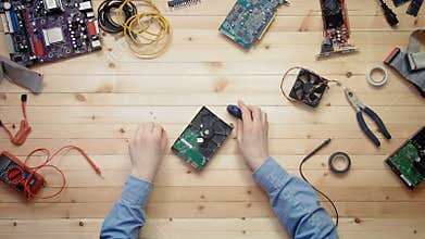 Top view computer technician repairing hard drive at wooden desk with tools and electronic components
