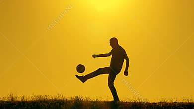 Football player practicing with the ball at sunset