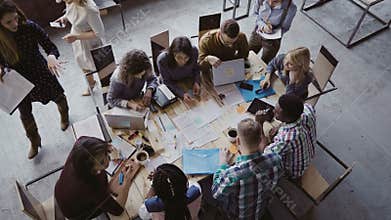 Top view of mixed race business team sitting at the table at loft office and working. Woman manager brings the document.