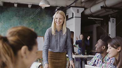 Beautiful blonde woman manager giving direction to multiethnic team. Creative business meeting at modern hipster office.