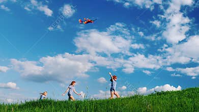 Carefree children play with a kite. Running along the green hill against the blue sky with white clouds. Happy childhood