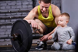 Young smiling father shows little son the dumbbell against brick wall at the cross fit gym.