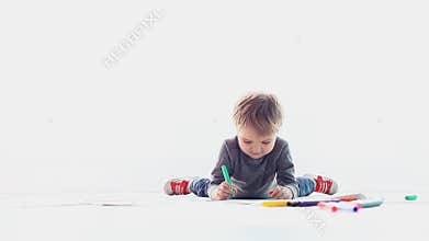 A boy sits on a white floor and draws