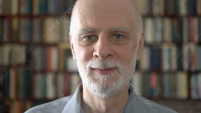 Portrait of good-looking handsome smiling senior man at home. Bookcase bookshelves in background