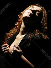 Sensual woman with red hair in dramatic low key light lifting face towards darkness with emotional expression