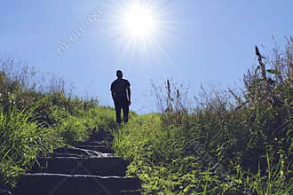 Silhouette of man walking up a stair towards the sun