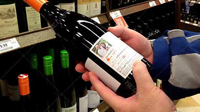 Man reading lable of red wine from the shelf.