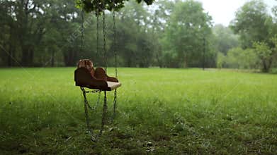 Empty wooden swing swaying slowly in the rain