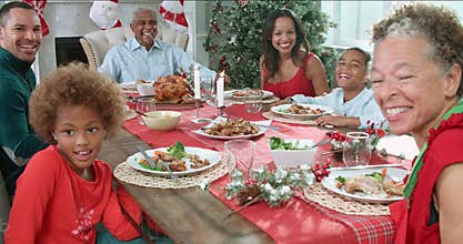 Slow motion sequence of family with grandparents sitting around table and enjoying Christmas meal - looking at camera
