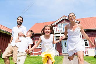 Happy family running on meadow in front of house