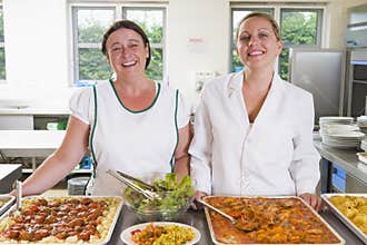 Lunchladies beside trays of food in a school