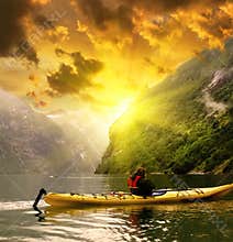 Kayaker eaves Geiranger fjord bay at rainy day in Norway