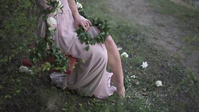 Young woman dressed in light pinc tunic playfully exposing her leg, sitting on decorated with flowers swing