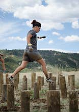 Female competitor running across tall wooden stumps