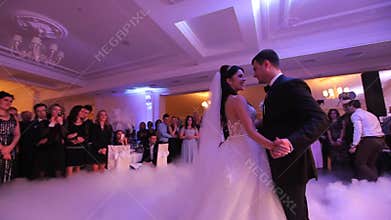 Beautiful young newlyweds dancing their first dance shrouded by white fume. Wedding celebration in the restaurant
