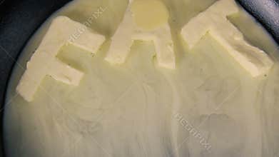 Butter in shape of the word fat melting on hot pan - Close up top view