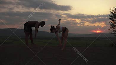 Silhouettes of athletic mixed race couple stretching together on the rocky mountains background. Sport fitness concept
