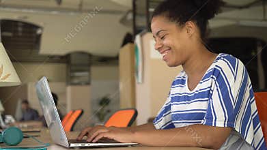Happy mixed race woman typing on the computer at the working place.