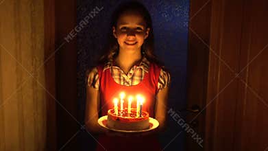 Girl carries the birthday cake with candles from the darkness