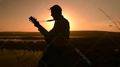 Young caucasian muician playing guitar outdoors at sunset time