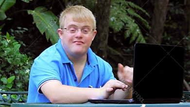 Handicapped young man typing on laptop in garden.