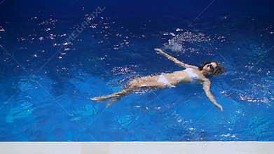 Slender girl in a white bathing suit floating on her back in the pool. Beautiful young woman enjoying vacation at the